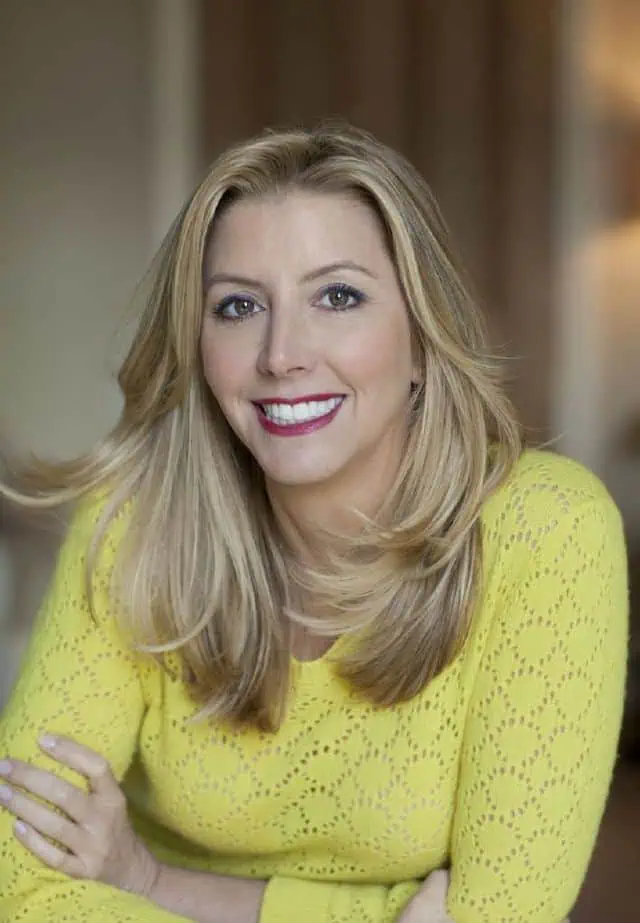 Sara Blakely, wearing a bright yellow sweater, smiles confidently, embodying the idea that not knowing can be a strength, encouraging unique and different approaches.
